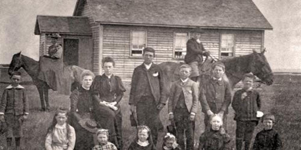 Group of people (adults & children) standing in front of old school
